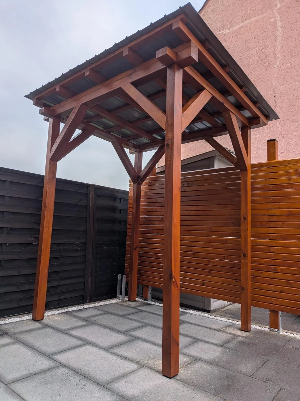 Holzpavillon mit Sichtschutzwand auf einer gepflasterten Terrasse